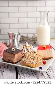 White Square Plate With Mini Sweet Cakes With Chocolate Mousse Cream Lemon Pai With Meringue Brownie With Bottle And Glass Of Milk Decorated With Dry Flowers