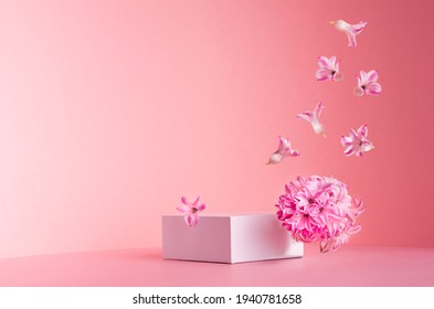 White square podium for display cosmetic   goods and hovering flow fresh spring flowers  gentle pastel pink background  copy space  modern fashion style 