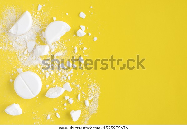 White squashed and broken round pills on yellow\
background. Crushed tablets. Medicine, pharmacy concept. Copy\
space. Flat lay