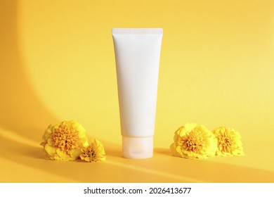 White squeeze bottle cosmetic cream tube and marigolds flowers on yellow background with shadow. Front view. Unbranded lotion, balsam, hand creme, toothpaste, moisturizer mockup. Clean beauty concept.