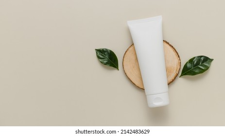 White Squeeze Cosmetic Tube For Cream On Wooden Stand With Plant Leaves, Copy Space, Product Mockup For Logo And Branding. Eco Friendly Organic Skin Care Cosmetic