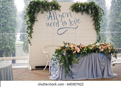 White Stand With Lettering 'All You Need Is Love' Stands Behind Blue Table For Newlyweds