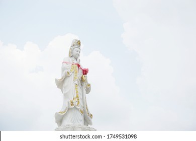 A white statue of the Lady Buddha or Guan Im standing on lotus base with sky background. Chinese god in Thailand. Mercy and Wealthy.