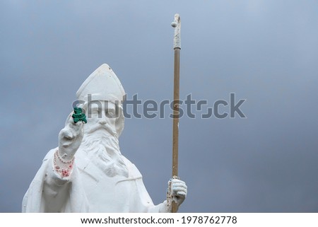 White statue of Saint Patrick holding green shamrock at the start of foot path to the peak of Croagh Patrick, county Mayo, Ireland.