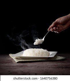 White steam rice with hand holding spoon eating hot rice over dark background