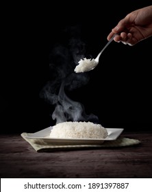 White Steam Rice With Hand Holding Spoon Eating Hot Rice Over Dark Background