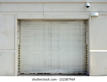 A White Steel Overhead Door In An Exterior Wall With Light Fixture And Security Camera