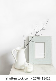 White Still Life. Scented Candle And Empty Photo Frame Mockup On Marble Table. Vase With A Branch. Scandinavian Interior Design. Front View. Copy Space