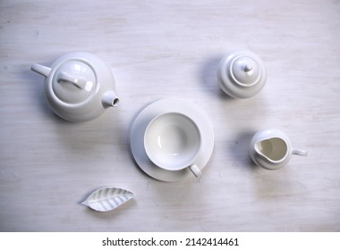 white still life with  tea cup and saucer, teapot, milk jug, creamer, sugar bowl  on  wooden table