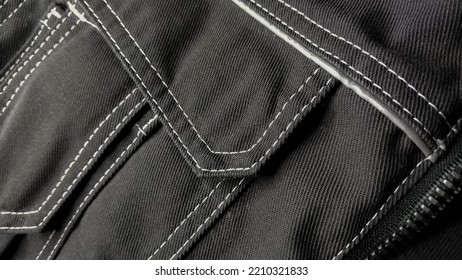 White Stitching On Black Fabric. Texture Black Working Clothes With White Stitching Closeup, Green Reflective Elements