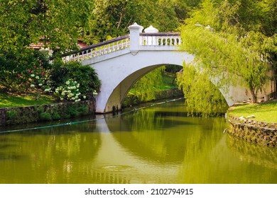 White stone arched bridge among dense greenery over the rippled river in a summer park on a sunny day