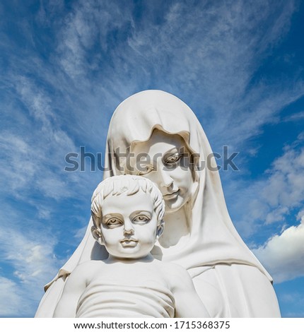A white stone statue of the Madonna and Jesus under nice sky