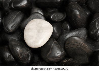 A white stone surrounded by other black stones for a conceptual difference.