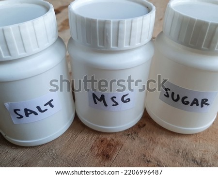 white storage jars of salt, MSG and sugar placed on a wooden table. seasoning that is always used when cooking.
