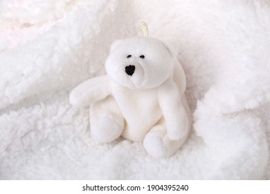 A White Stuffed Polar Bear On A Fur White Blanket.