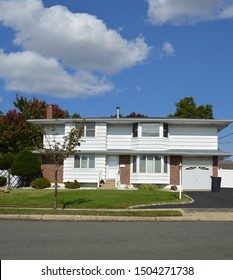 White Suburban High Ranch Home With Brick And Black Garbage Can In Driveway USA Blue Sky Clouds