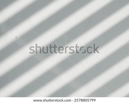 white surface with diagonal shadows cast across it. The shadows are created by light passing through a set of parallel slats or blinds, resulting in a pattern of alternating light and dark stripes