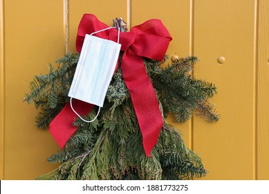 A white surgical mask hangs with a red bow on a decorative display of boughs of pine branches during the pandemic on Christmas Eve, 2020, Monterey CA. - Powered by Shutterstock