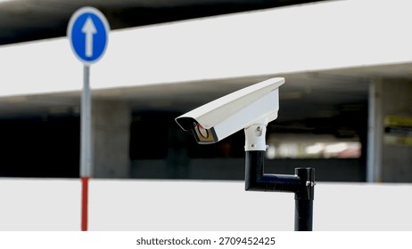White surveillance camera facing forward, mounted outdoors near a one-way street sign, symbolizing urban monitoring and traffic security.