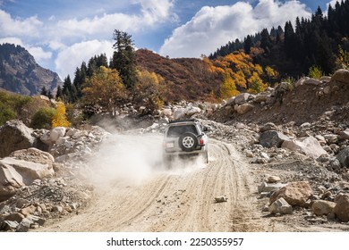White SUV car climbs a dusty road in the autumn mountains.