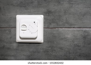White Switch And Underfloor Heating Thermostat On A Gray Concrete Wall In A Modern Bathroom