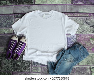 White T Shirt Mockup Flat Lay On Purple Brick Background With Purple Shoes And Ripped Jeans