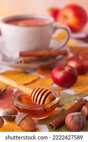 White Table With Autumn Decorations, A Cup Of Tea, Cinnamon Pieces, A Glass Bowl With Honey, Small Apples, Nuts, Colourful Tree Leaves And Acorns. Low Angle Of View, No People.