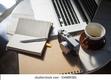 White table with a cup of coffee ,camera and laptop