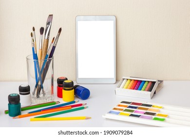 White table with digital tablet with blank screen on white table with colorful drawing supplies