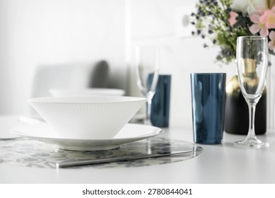 White table with elegant tableware, blue glasses and flower vase in bright modern apartment interior.