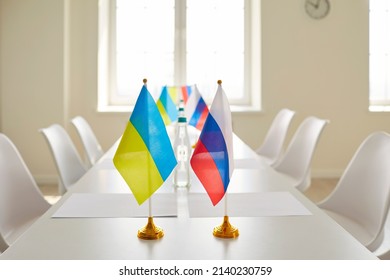 White Table With Flags Of Ukraine And Russia In Empty Negotiation Room. Office Interior Before Meeting Of Diplomats Who Are Going To Work Towards Ending War And Conflict Resolution. Nobody, No People