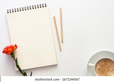 White table at home. Open empty sketchbook, wooden pencils and an orange-red carnation. Cocoa with foam in a white cup. Mockup. Creative desk - Shutterstock ID 1671244567