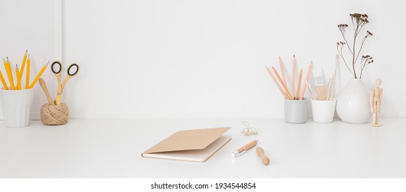 White table, organised desk, with many pencils, supplies, notebook on the center. Creative workspace.