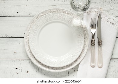White table setting from above. Elegant empty plate, cutlery, napkin and glass on shabby chic or vintage planked wood table.