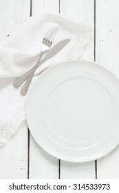 White Table Setting From Above. Empty Plate, Cutlery, Napkin On Planked Wood Table.