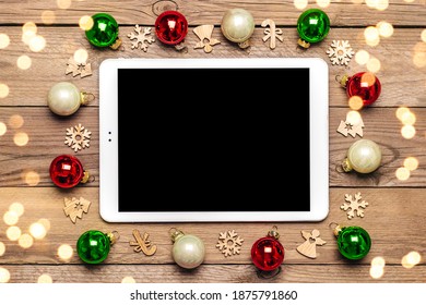 White tablet with black screen, bauble, lights, Christmas decor on  wooden table Top view Flat lay Distance congratulations to family,  friends, online shopping concept Holiday card 2021 New Year