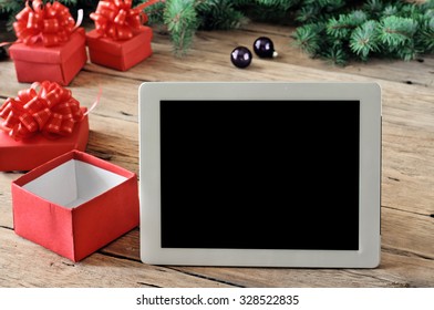 White tablet computer with open Christmas gifts on wooden table closeup. Copy space. Free space for text