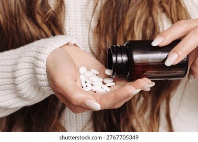 White tablets falling from a dark bottle into an open hand. Medication and dosage concept. Closeup of pharmaceutical routine, supplement use and healthcare treatment indoors with soft light.
