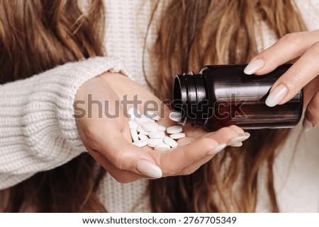 White tablets falling from a dark bottle into an open hand. Medication and dosage concept. Closeup of pharmaceutical routine, supplement use and healthcare treatment indoors with soft light.