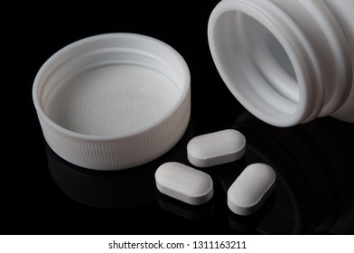 White Tablets Of Medicine And Pills Bottle With Opened Cap On Black Background; Safe Drug Use And Medical Treatment Concept