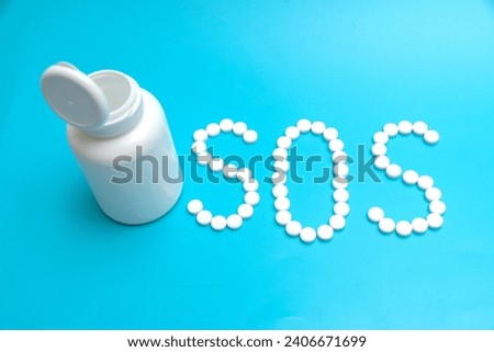 White tablets on a blue background laid out in the form of letters SOS. The concept of medical treatment in an emergency situation.