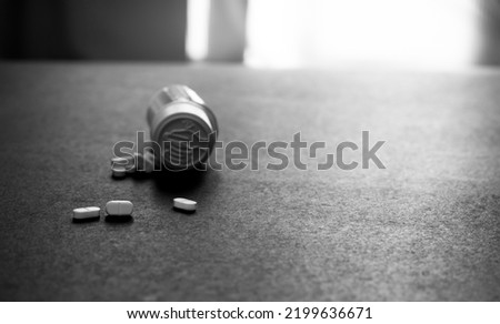 White tablets pills and blur plastic pill bottle on dark floor. Prescription drugs. Pharmaceutical industry. Medical care. Medication for mental illness. Pharmacy. Small white pills. Dose recommended.