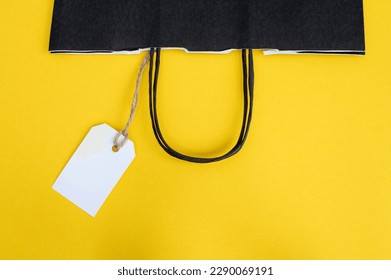 White tag with a paper black bag for recycling on a yellow background. Paper bag handles. Price label. Place for text. copy space - Powered by Shutterstock