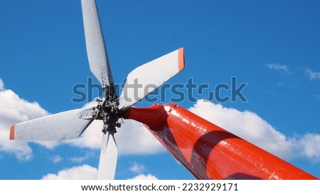 The white tail rotor of a bright red helicopter against a cloudy blue sky. Propeller on tail of a red multi-purpose twin-engine helicopter. White tail rotor with red stripes at the ends of the blades.