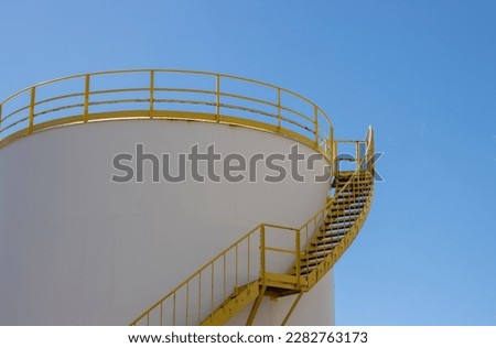 White tank with yellow staris and railing on the top. Bright blue sky. Part of the industrial zone in the capital city. Puerto del Rosario, Fuerteventura, Canary Islands, Spain.