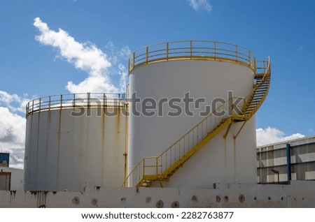 White tanks with yellow staris and railing on the top. Bright blue sky with white clouds. Part of the industrial zone in the capital city. Puerto del Rosario, Fuerteventura, Canary Islands, Spain.
