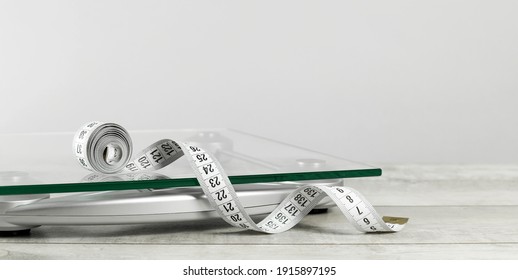 white tape measure on top of glass bathroom weighing scale on blue. Front view copy space. Healthy lifestyle, weight losing management and hydration concept banner - Powered by Shutterstock