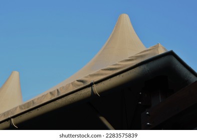 white tarpaulin taut, shading from the sun and rain over the terrace of the restaurant, on the playground in the kindergarten, on the platform. just a mast and taut, wood collumn, post blue sky