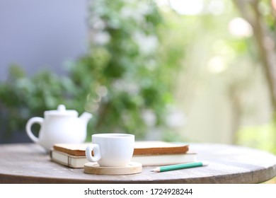 White Tea Kettle And White Cup With Notebook And Pencil On Wooden Table Outdoor View
