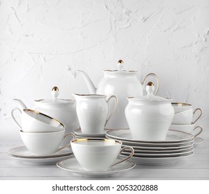 White tea set on a white background. Teapot, cream, sugar bowl, cups, saucers, plates on the table. Porcelain dishes. For six persons.
				